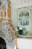 Stone-clad fireplace and chimney breast next to small vintage cabinet mounted on white wooden wall