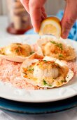 A Hand Squeezing Lemon onto Baked Scallops