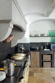 Vintage kitchen counter with worksurface and splashback in black stone below masonry extractor hood in rustic kitchen with arched niche in wall