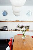 Drei Bullaugen über Küchenzeile mit einfachem Gläserbord und Hängelampen mit Papierschirm über Esstisch