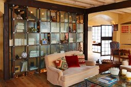 Two-seater couch with colourful scatter cushions in front of partition shelving with glass doors in open-plan interior