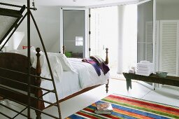 Moderner, offener Schlafbereich mit antikem Bett gegenüber offener Terrassen-Flügeltür und teilweise sichtbarer Teppichläufer mit bunten Streifen
