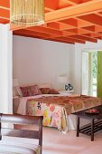 Orangerot gestrichene Deckenkonstruktion über Doppelbett mit floral gemustertem Bezug