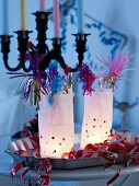 Paper-bag lanterns with party decorations on metal dish in front of multi-armed candlestick