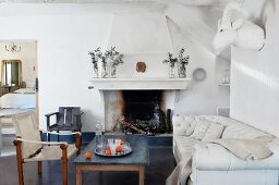 Soot-blackened fireplace, table, sofa, chairs and animal head sculpture on wall in renovated country house