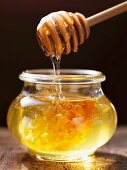 Honey dripping from a honey spoon into a jar