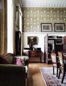 Grandiose dining room with patterned wallpaper and stucco ceiling and curved back, antique sofa on a wall across from the dining area in front of an open double door