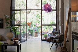 Künstlerischer Möbel- und Objektemix im Loft vor Fensterfront mit Blick auf begrünte Terrasse