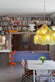 Designer chandelier above dining area; bookcases above kitchen counter with postmodern bar stools; sunken bathtub in background