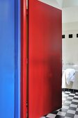 View through an open, red door into a bathroom with black and white checkerboard floor