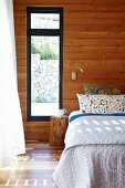 Double bed against wood-clad wall next to window