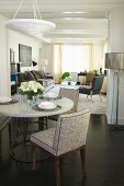 Set dining table and upholstered chairs below modern pendant lamp in front of wide doorway with view into living room beyond