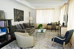 Armchairs and grey sofa around glass table on patterned rug and closed curtains at windows