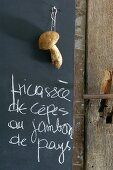 Handwritten menu and fresh penny bun mushroom hanging against blackboard in kitchen
