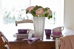Holztisch mit Geschirrstapel; in der Mitte ein dekorativer Blumenstrauss mit Ranunkeln
