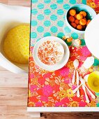 Im Hippie-Look, farbenfroh mit floral gemustertem Geschenkpapier selbst gestalteter Glastisch; Retro Schalenstuhl mit gelbem Kissen