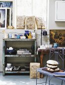 Delicate, blue metal bench in front of vintage shelves with peeling paint against half-height wall and window in workshop-style interior
