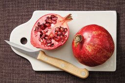 A whole and a half pomegranate on a chopping board with a knife