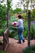View through open garden gate of woman walking through wild cottage garden holding bouquet