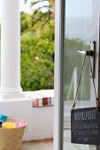 Open glass door with a sign hanging from it and a view of the terrace with antique columns in front of the garden