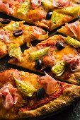 Pizzastücke mit Pancetta, Artischocken und schwarzen Oliven