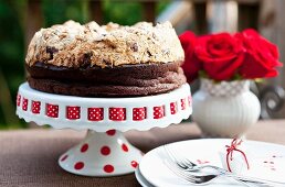 Schokoladen-Haselnuss-Kuchen mit Baiserhaube auf Kuchenständer, rote Rosen in einer Vase