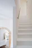 Staircase with modern handrail as reductionist, white spatial sculpture next to historical, stone arched doorway leading to dining area