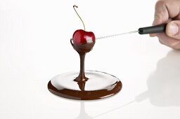 A cherry being dipped in melted chocolate