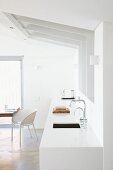 Designer-style white kitchen counter below sloping ceiling and white shell chair in front of French doors