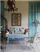 Country-style sofa with various scatter cushions, wicker chair and narrow coffee table; folk art pictures flanked by closed door shutters