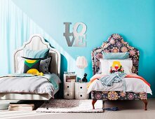 Matching twin beds in children's bedroom with curved headboards and different upholstery; mirrored letters spelling 'Love' and ecru rug as connecting elements