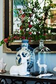 Hirschfiguren aus weißem Porzellan und Keramikvase mit blühenden Zweigen vor elegantem Spiegel