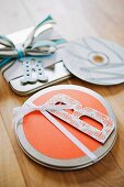 Flat metal tins covered in wrapping paper and decorated with large ornamental letters