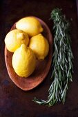 Zitronen in einer Holzschale, daneben Rosmarin