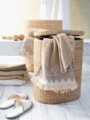 Towel draped over laundry basket next to slippers and stacked towels on white wooden floor