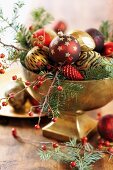Weihnachtskugeln auf Tannen- und Beerenzweigen in vergoldeter Schale