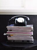 Retrotelefon auf Zeitschriftenstapel vor schwarz gestrichener Wand