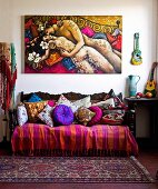 Antique sofa with colourful collection of blankets and cushions below painting of couple embracing