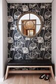 Round, latticed window on floral wallpaper and bench with black leather seat cushion in niche