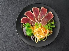 Tuna sashimi with sesame seeds, carrot strips and wide noodles