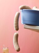 Raw white sausages hanging over the edge of a blue plastic bowl
