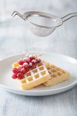 Waffles with redcurrants being dusted with sugar