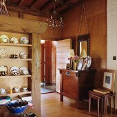 Open-plan dining area with crockery on rustic shelving and cabinet against wood-panelled wall