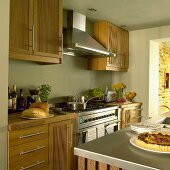 Küche im Landhausstil mit pastellgrünen Wänden, Holzmöbeln, Dunstabzugshaube über dem Herd und Mittelblock mit Spülbecken