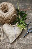 Still-life arrangement of hand-sewn, heart-shaped hessian sachet, reel of yarn and vintage scissors on wooden surface