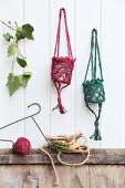 Lantern holders hand-crocheted from dyed jute yarn hanging on white wood panelling