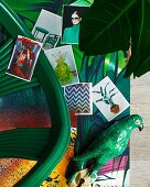 Various photos and artistic parrot figurine on colourful surface with jungle pattern