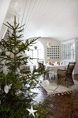 Mit weissen Sternen und Glaskugeln dekorierter Weihnachtsbaum; Esszimmer mit holzverkleideter, weisslackierter Tonnendecke und Mosaikparkett