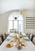 Table festively set in delicate colours; dining room with luster of glass bubbles hanging from vaulted, wooden ceiling and arched window