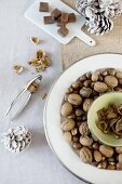 Festive table arrangement in natural shades with nuts on pale plates with silver rims, squares of chocolate on china board and white fir cones